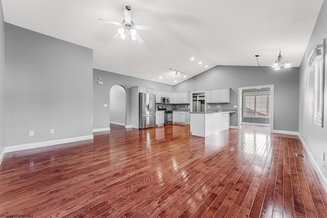 unfurnished living room with baseboards, vaulted ceiling, arched walkways, dark wood-style floors, and a ceiling fan