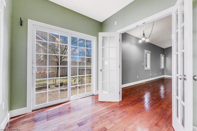 spare room featuring a chandelier, baseboards, and hardwood / wood-style floors