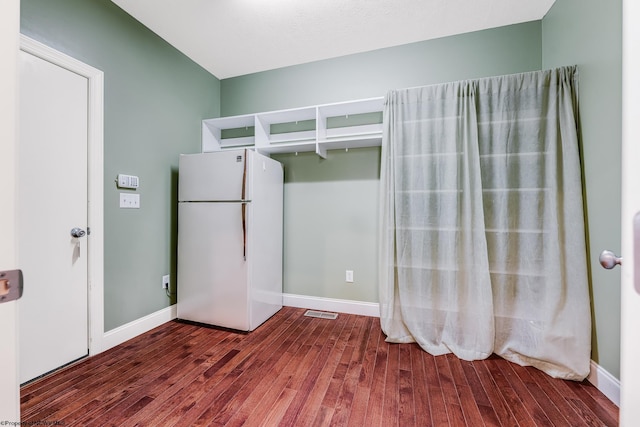 unfurnished bedroom with baseboards, wood finished floors, and freestanding refrigerator