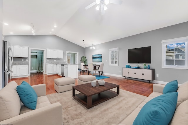 living room with baseboards, lofted ceiling, a ceiling fan, and light wood finished floors