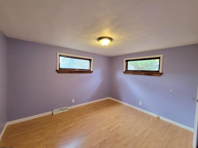 empty room featuring visible vents, plenty of natural light, baseboards, and light wood finished floors