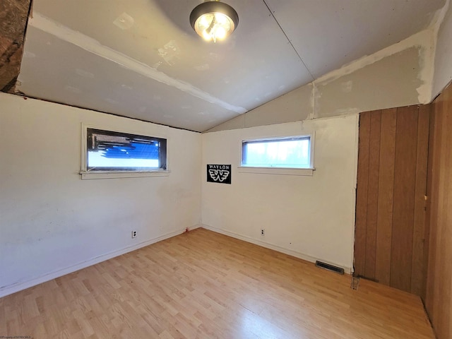 empty room with visible vents, light wood-type flooring, baseboards, and vaulted ceiling