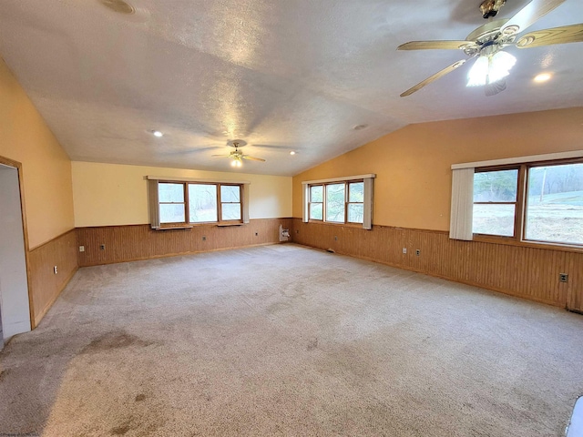 spare room featuring lofted ceiling, ceiling fan, wainscoting, and wood walls