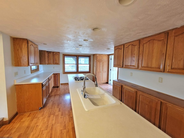 kitchen featuring a textured ceiling, brown cabinetry, light wood finished floors, and a sink