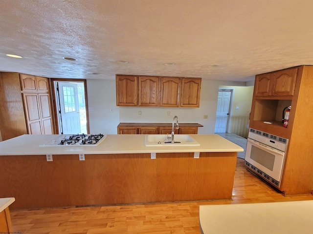 kitchen with brown cabinets, a sink, a kitchen breakfast bar, white appliances, and light wood finished floors