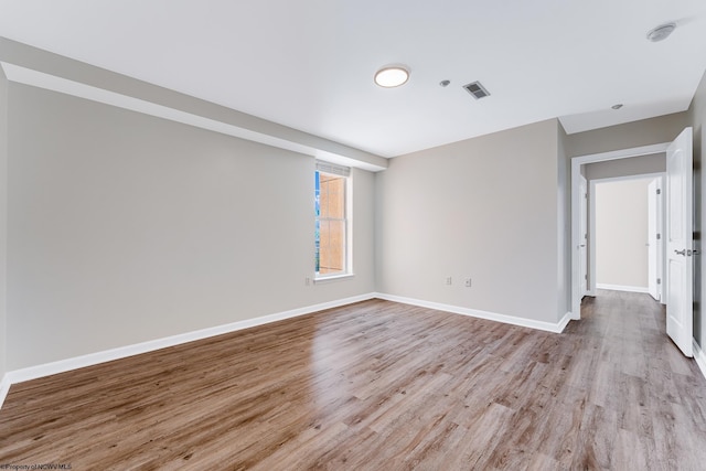 spare room with wood finished floors, visible vents, and baseboards