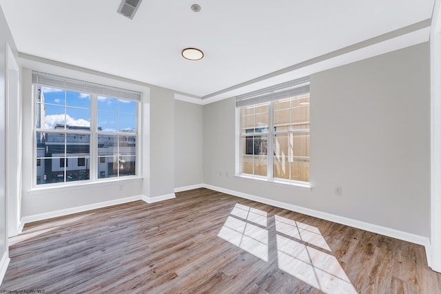 unfurnished room with wood finished floors, visible vents, and baseboards