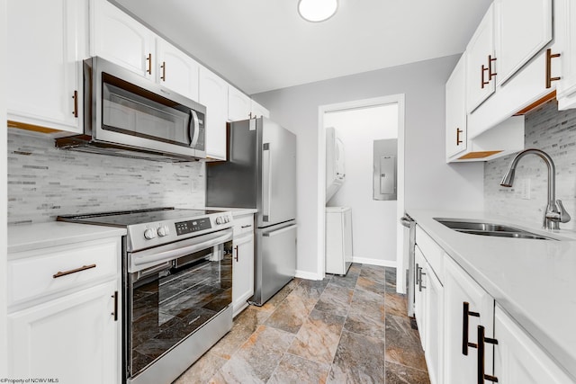 kitchen featuring baseboards, stacked washer and dryer, appliances with stainless steel finishes, stone finish floor, and a sink