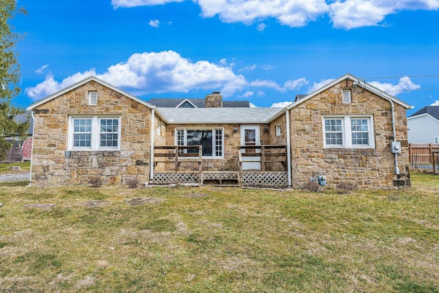 view of front facade with stone siding, a chimney, a deck, and a front yard