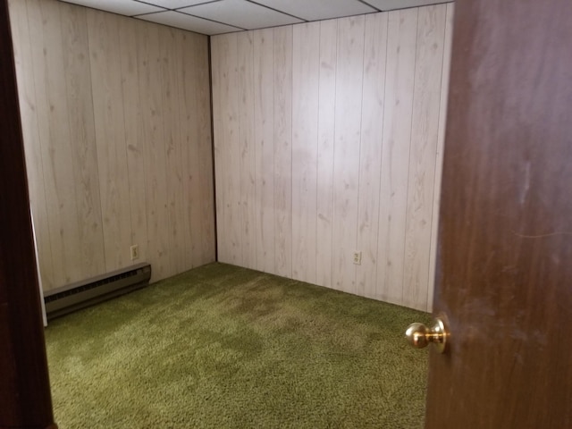 empty room with a paneled ceiling, a baseboard heating unit, carpet floors, and wooden walls