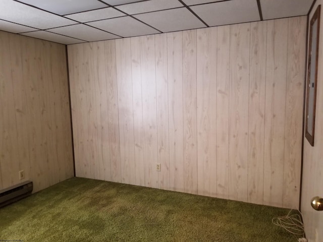 carpeted empty room with baseboard heating, a drop ceiling, and wood walls