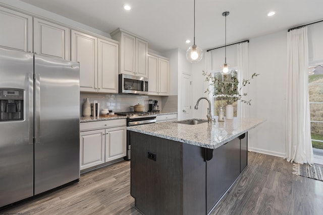 kitchen with dark wood-type flooring, light stone countertops, decorative backsplash, appliances with stainless steel finishes, and a sink