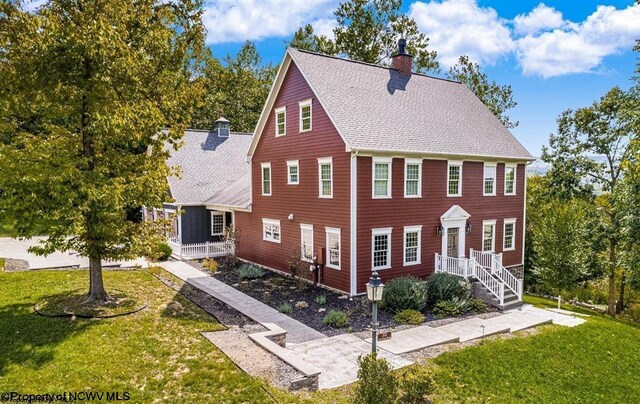 colonial home featuring a chimney, a front lawn, and a shingled roof