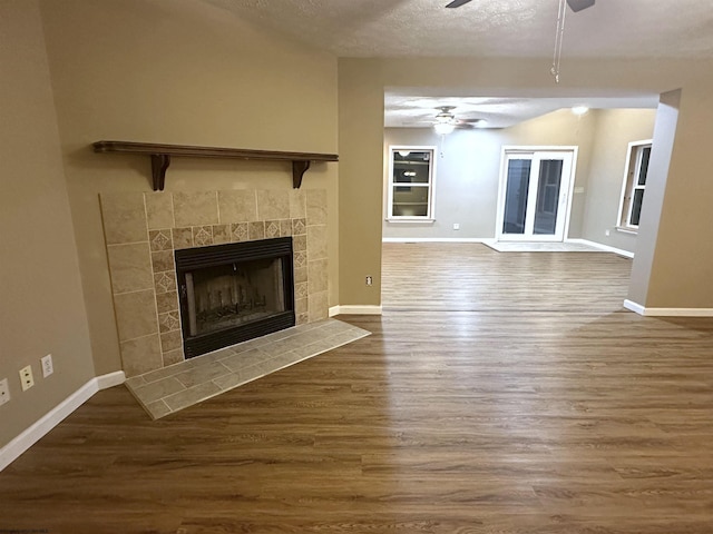 unfurnished living room featuring a fireplace, wood finished floors, a ceiling fan, and baseboards