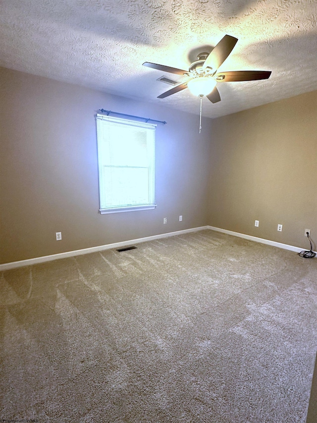 carpeted spare room with a textured ceiling, baseboards, visible vents, and ceiling fan