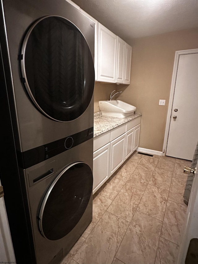 laundry room with a sink, baseboards, cabinet space, and stacked washer and dryer