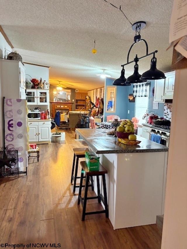 6615 Old Mill Rd, Jane Lew, WV 26378 - kitchen featuring dark countertops, stainless steel range with gas stovetop, wood finished floors, white cabinets, and a textured ceiling