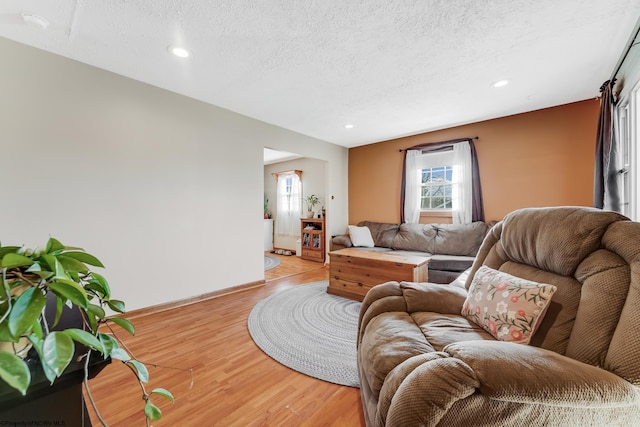 living area featuring recessed lighting, baseboards, light wood-style floors, and a textured ceiling