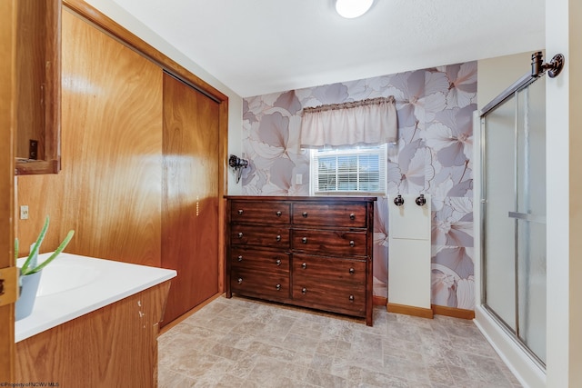 bathroom featuring a stall shower, wallpapered walls, vanity, and baseboards