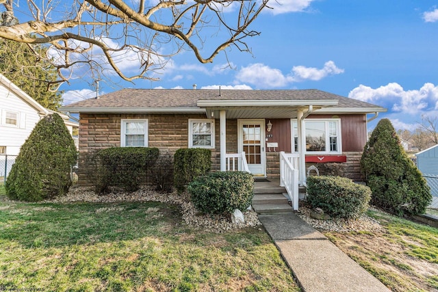 view of front of house featuring a front yard, fence, stone siding, and a shingled roof