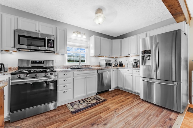 kitchen with light wood-type flooring, a sink, a textured ceiling, stainless steel appliances, and light stone countertops