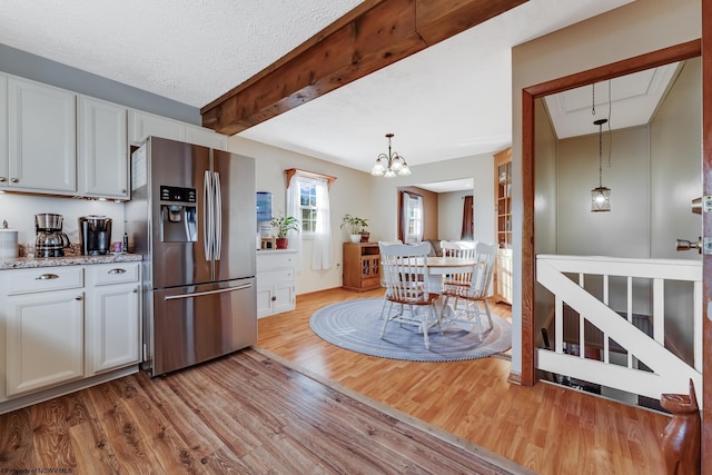 kitchen featuring stainless steel fridge with ice dispenser, decorative light fixtures, light wood-type flooring, beam ceiling, and a textured ceiling