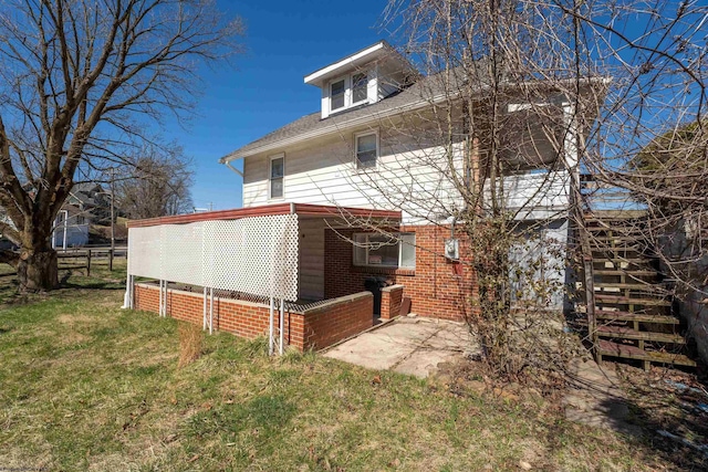 rear view of house featuring a shingled roof, a patio, brick siding, and a yard