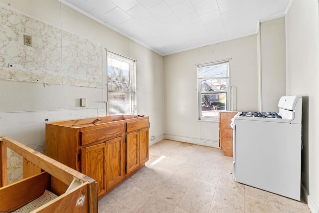 kitchen featuring white gas range oven, crown molding, brown cabinets, and a wealth of natural light