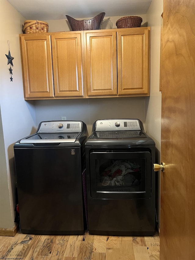 clothes washing area featuring washer and clothes dryer, light wood-style floors, and cabinet space