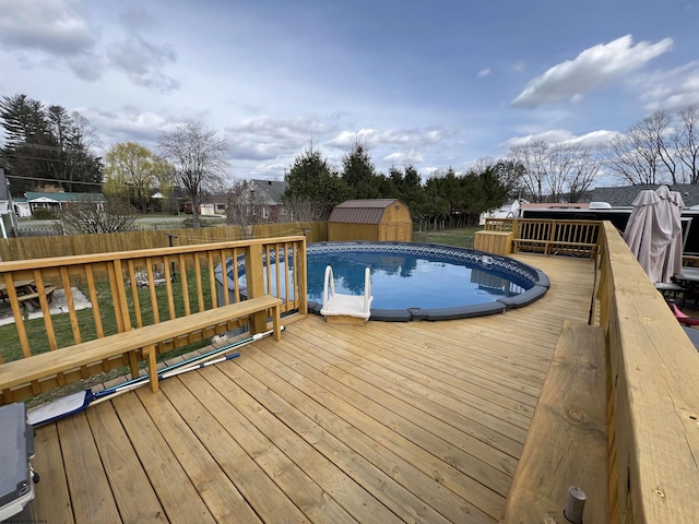 view of pool with an outbuilding, fence, a wooden deck, and a storage shed