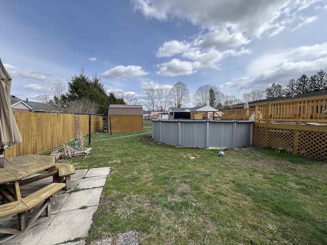 view of yard featuring a fenced in pool, a deck, an outdoor structure, a storage shed, and a fenced backyard