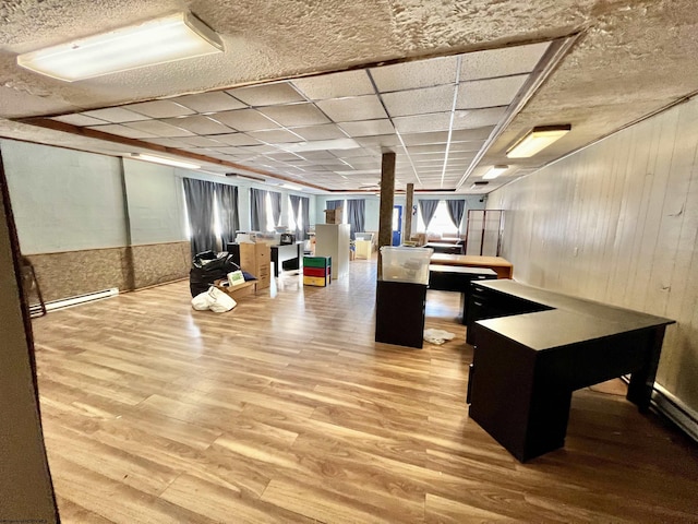 interior space with wood finished floors, a baseboard heating unit, a paneled ceiling, and wooden walls