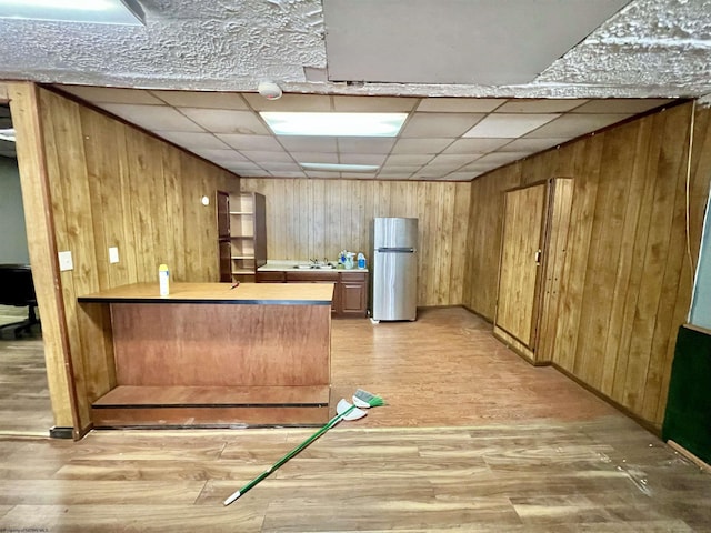kitchen with light wood-type flooring, wooden walls, a sink, and freestanding refrigerator