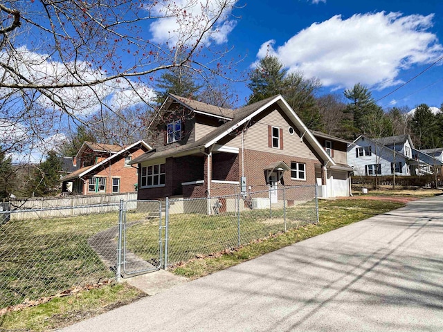 view of side of home featuring a gate, brick siding, a fenced front yard, a garage, and a yard