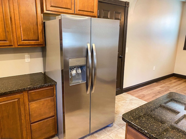 kitchen with baseboards, dark stone countertops, stainless steel fridge with ice dispenser, brown cabinetry, and light tile patterned floors