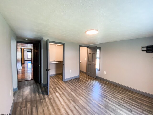unfurnished bedroom with multiple windows, a spacious closet, wood finished floors, and baseboards