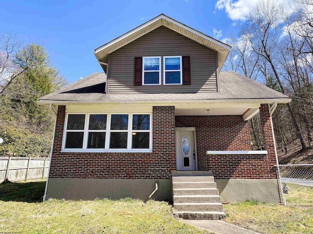 view of front of property featuring brick siding, a shingled roof, fence, and a front lawn