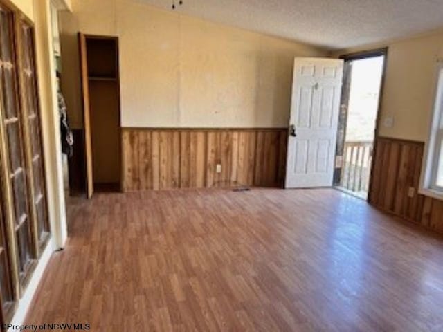 empty room with wood finished floors, a textured ceiling, wood walls, and wainscoting