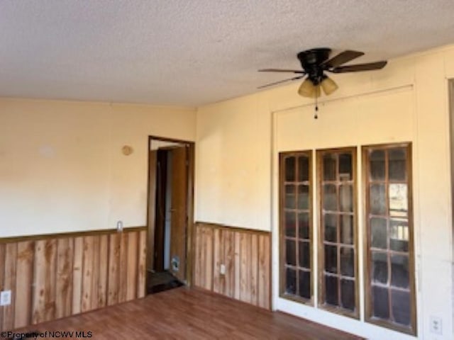 empty room featuring wainscoting, ceiling fan, and a textured ceiling