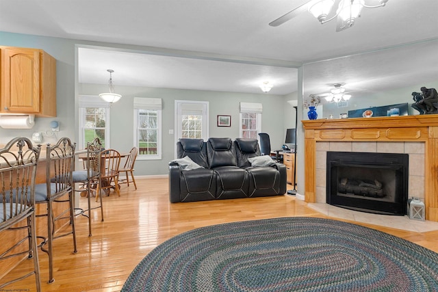 living area featuring baseboards, ceiling fan, a tile fireplace, and light wood finished floors