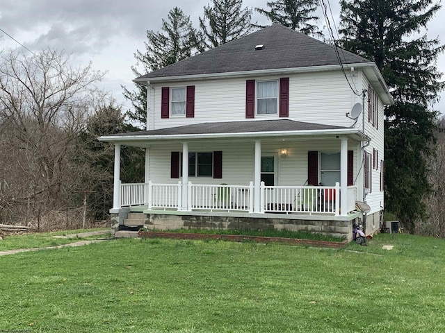 view of front facade with a front yard, central AC, a shingled roof, and covered porch