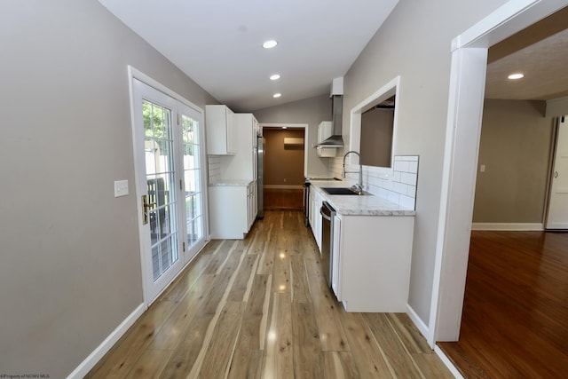 kitchen with tasteful backsplash, baseboards, a sink, wall chimney range hood, and light wood-style flooring