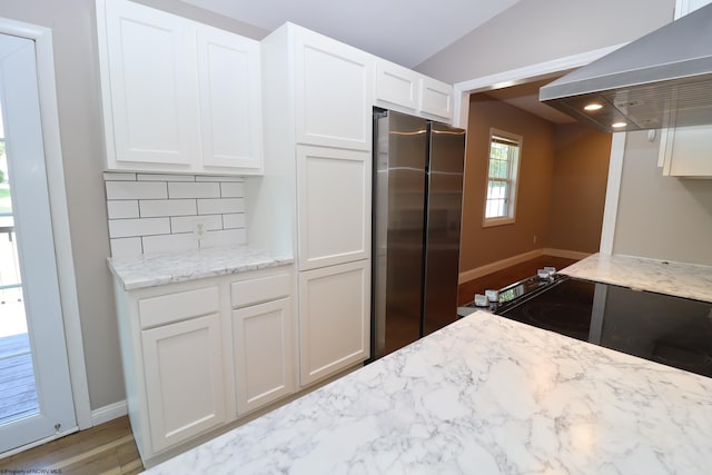 kitchen with decorative backsplash, white cabinets, light stone countertops, wall chimney range hood, and freestanding refrigerator