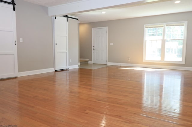 spare room with light wood finished floors, baseboards, a barn door, and recessed lighting
