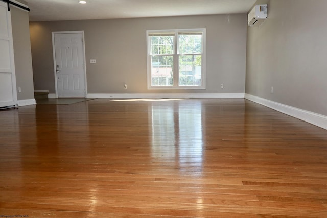 unfurnished room featuring baseboards, a barn door, an AC wall unit, and light wood-type flooring
