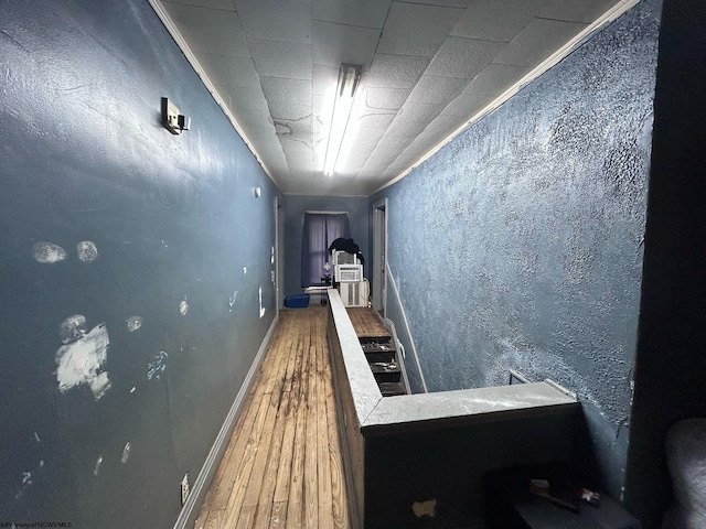 corridor featuring a textured wall, baseboards, and wood finished floors