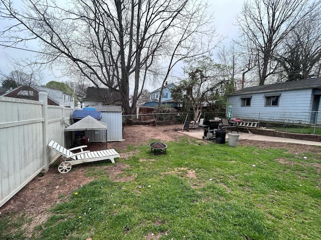 view of yard with a shed, a fire pit, a fenced backyard, and an outbuilding