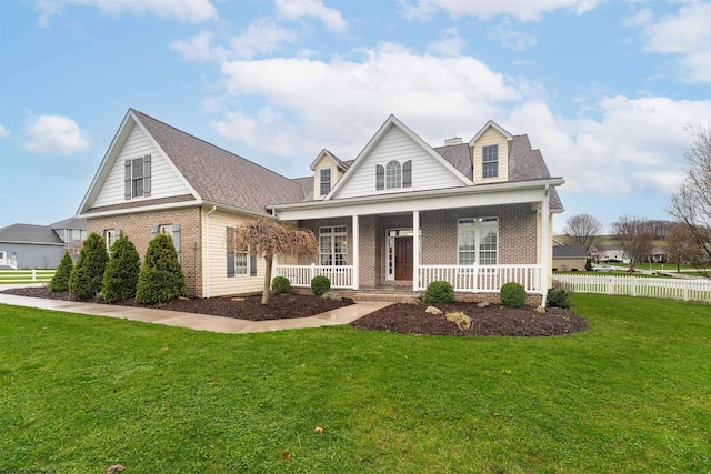 view of front of home with a porch, brick siding, fence, and a front lawn