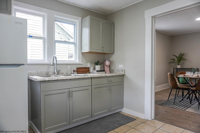 kitchen with freestanding refrigerator, gray cabinets, light tile patterned flooring, a sink, and light countertops