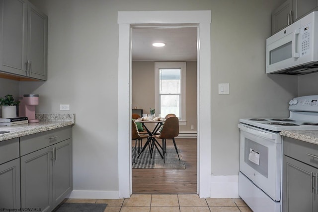 kitchen with baseboards, light stone counters, gray cabinets, white appliances, and light tile patterned floors